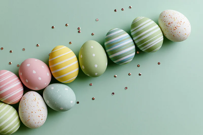 Pastel-painted easter eggs arranged in a loose diagonal row on a mint green surface with scattered glitter confetti