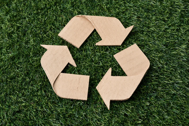 Recycling symbol cut from corrugated cardboard lying flat on green grass