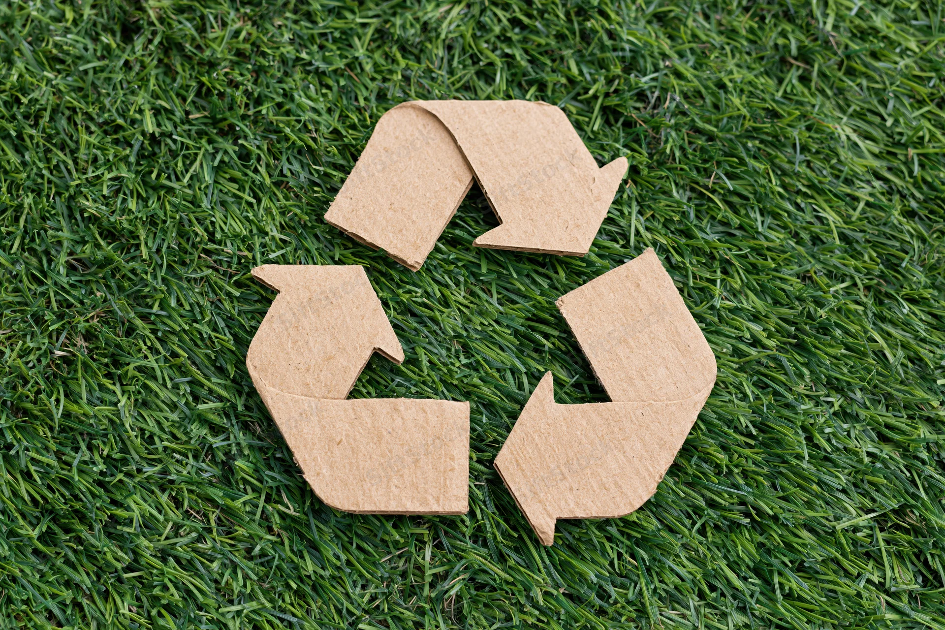 Recycling symbol cut from corrugated cardboard lying flat on green grass