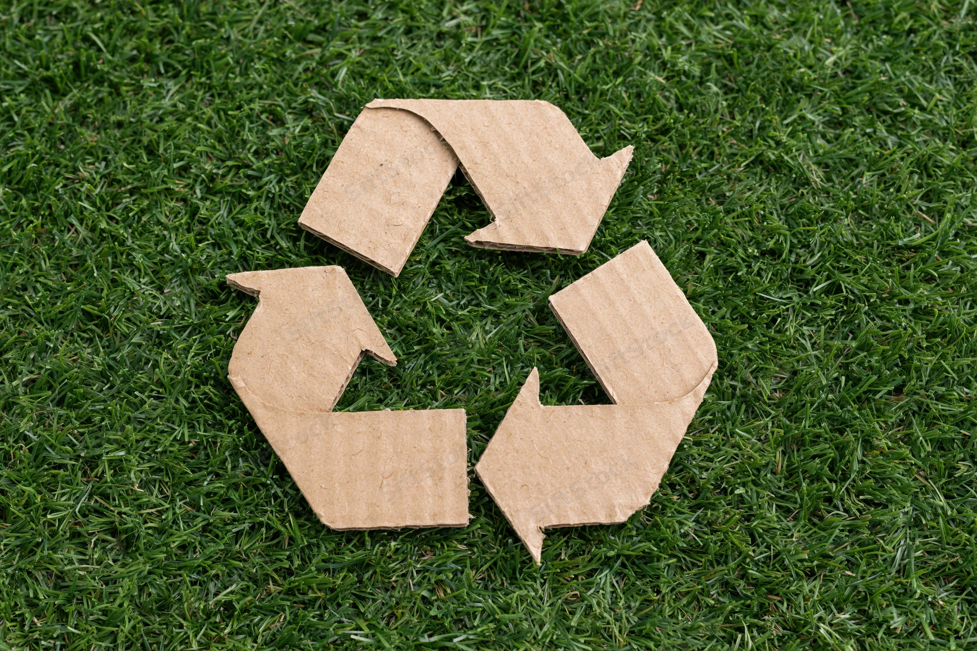 Recycling symbol cut from corrugated cardboard lying flat on green grass