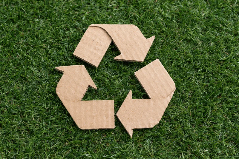 Recycling symbol cut from corrugated cardboard lying flat on green grass