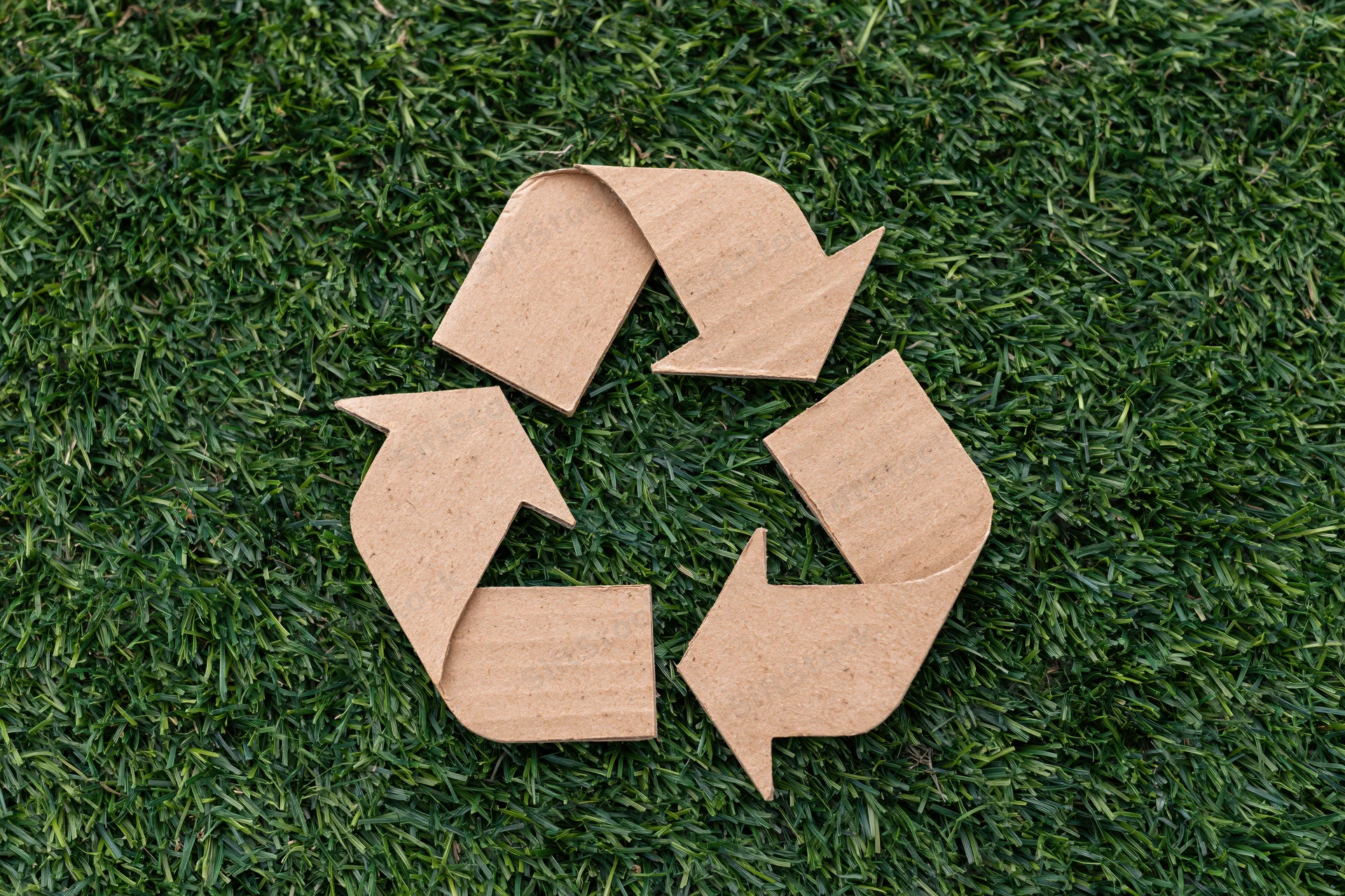 Recycling symbol cut from corrugated cardboard lying flat on green grass lawn