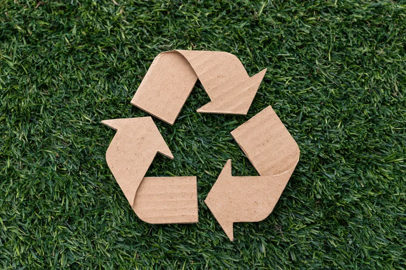 Recycling symbol cut from corrugated cardboard lying flat on green grass lawn