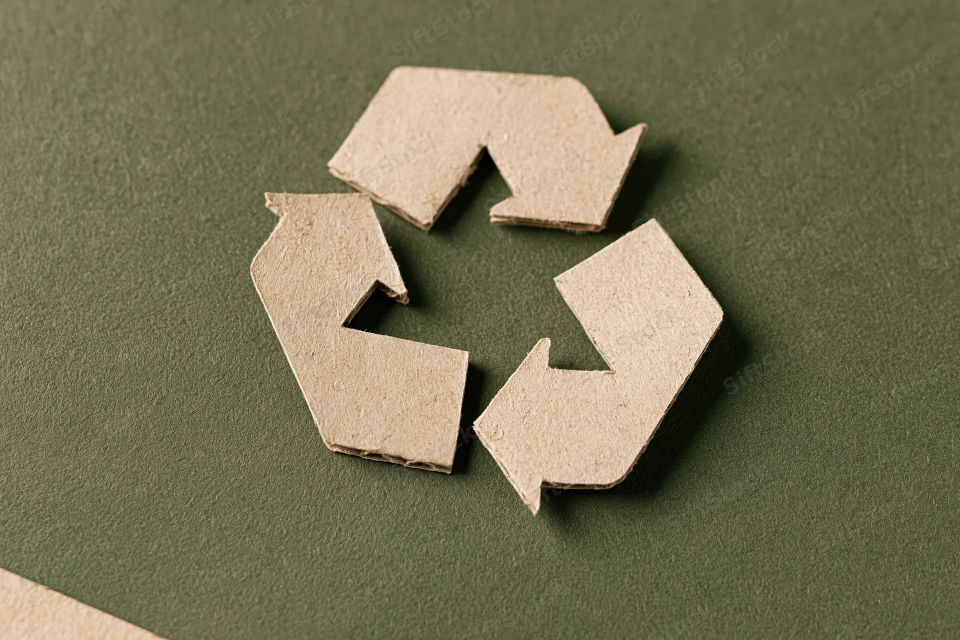 Recycling symbol cut from kraft cardboard paper placed flat on green background