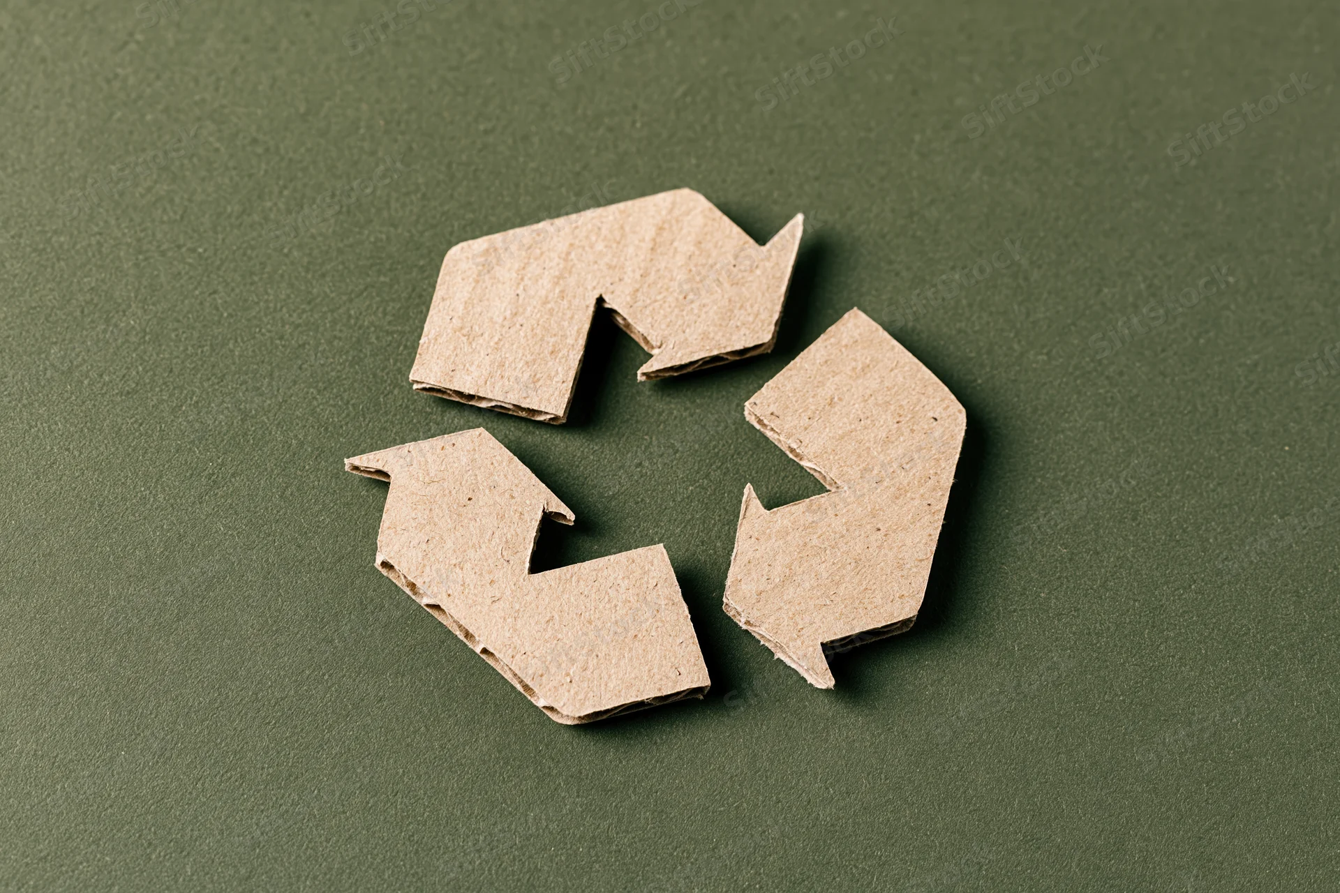 Recycling symbol cut from kraft cardboard paper placed flat on dark green surface
