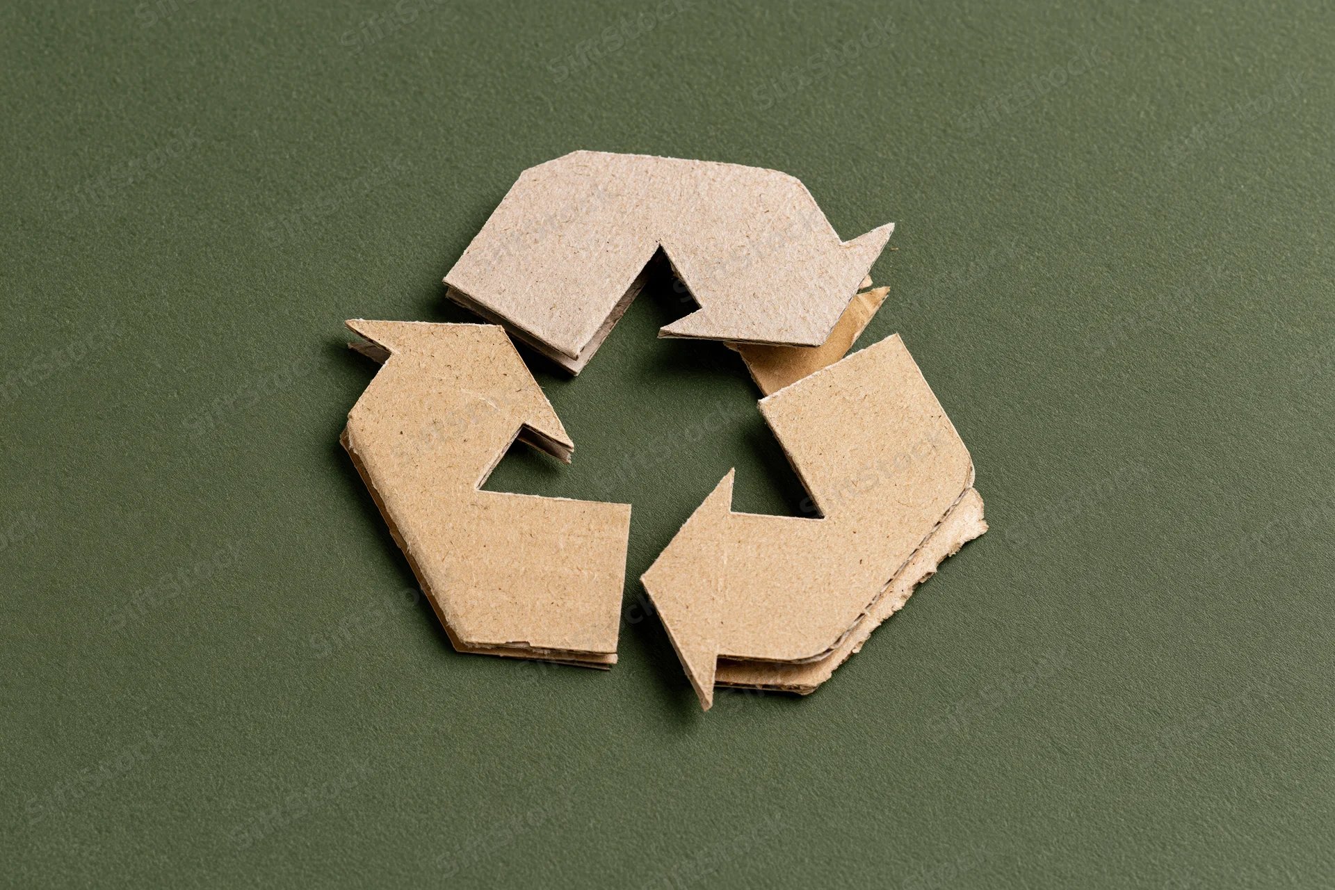 Recycling symbol cut from kraft cardboard paper placed flat on green background