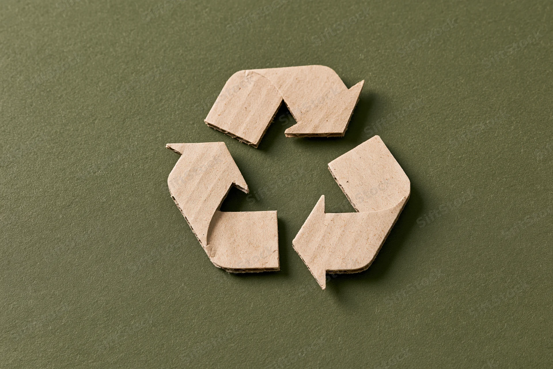 Recycling symbol cut from kraft cardboard paper placed flat on green background