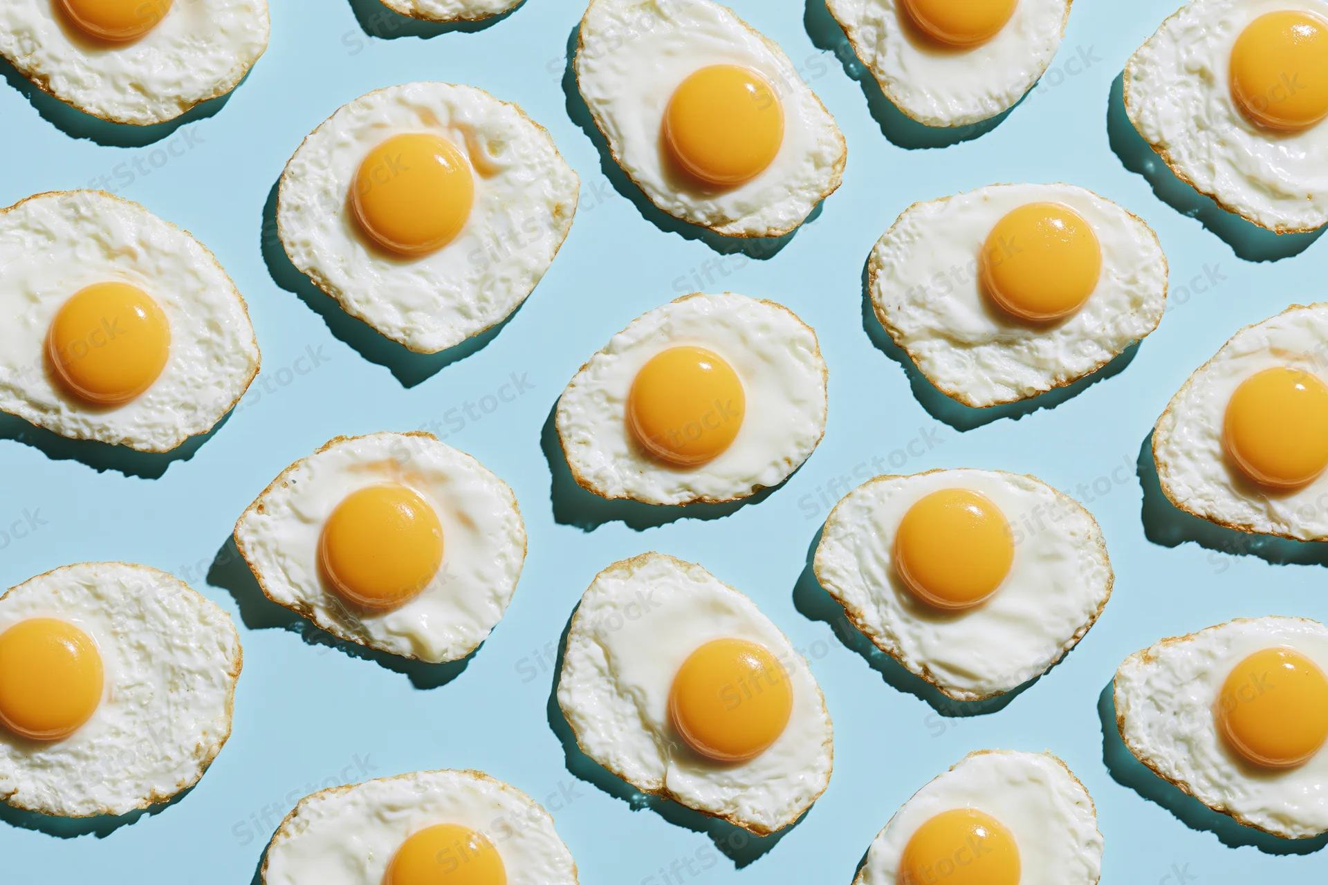 Fried eggs arranged in a repeating grid pattern on a light blue background