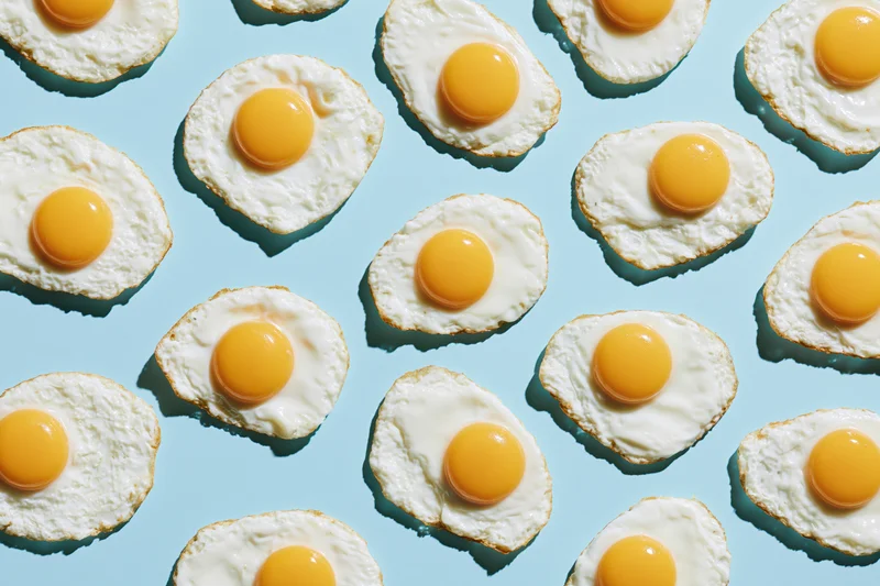 Fried eggs arranged in a repeating grid pattern on a light blue background