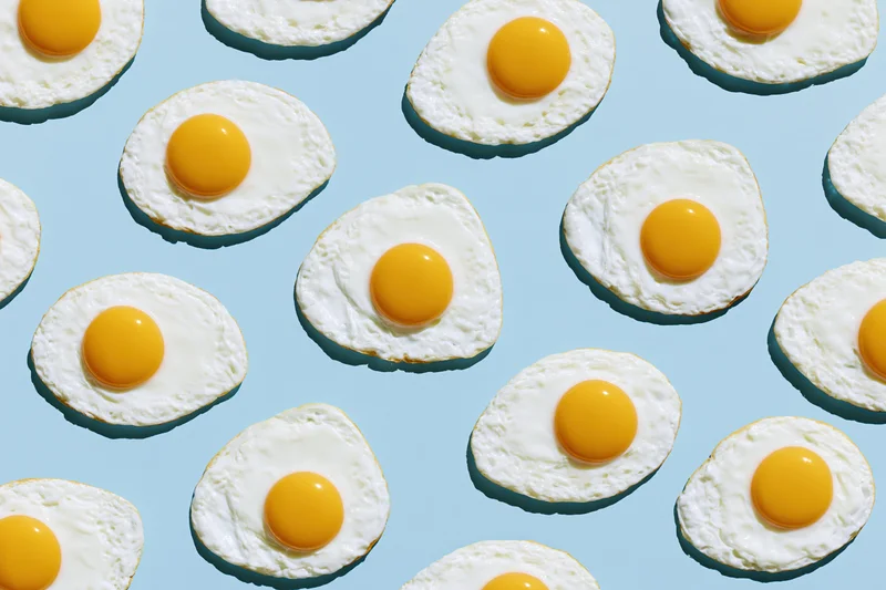 Fried eggs arranged in a repeating grid pattern on a blue background