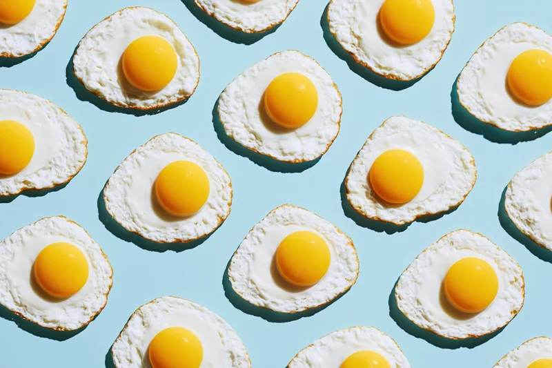 Fried eggs arranged in a repeating grid pattern on a blue background