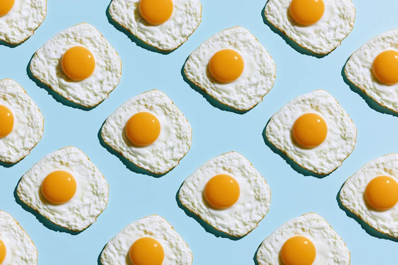 Fried eggs arranged in a repeating grid pattern on a light blue background