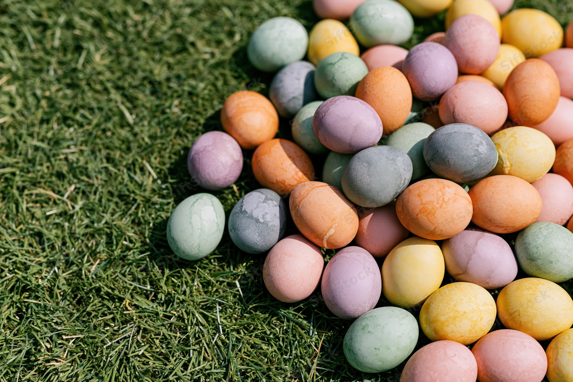 Hand-dyed easter eggs in pastel colors scattered on green grass outdoors