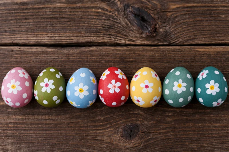 Seven hand-painted easter eggs arranged in a row on a rustic wooden surface