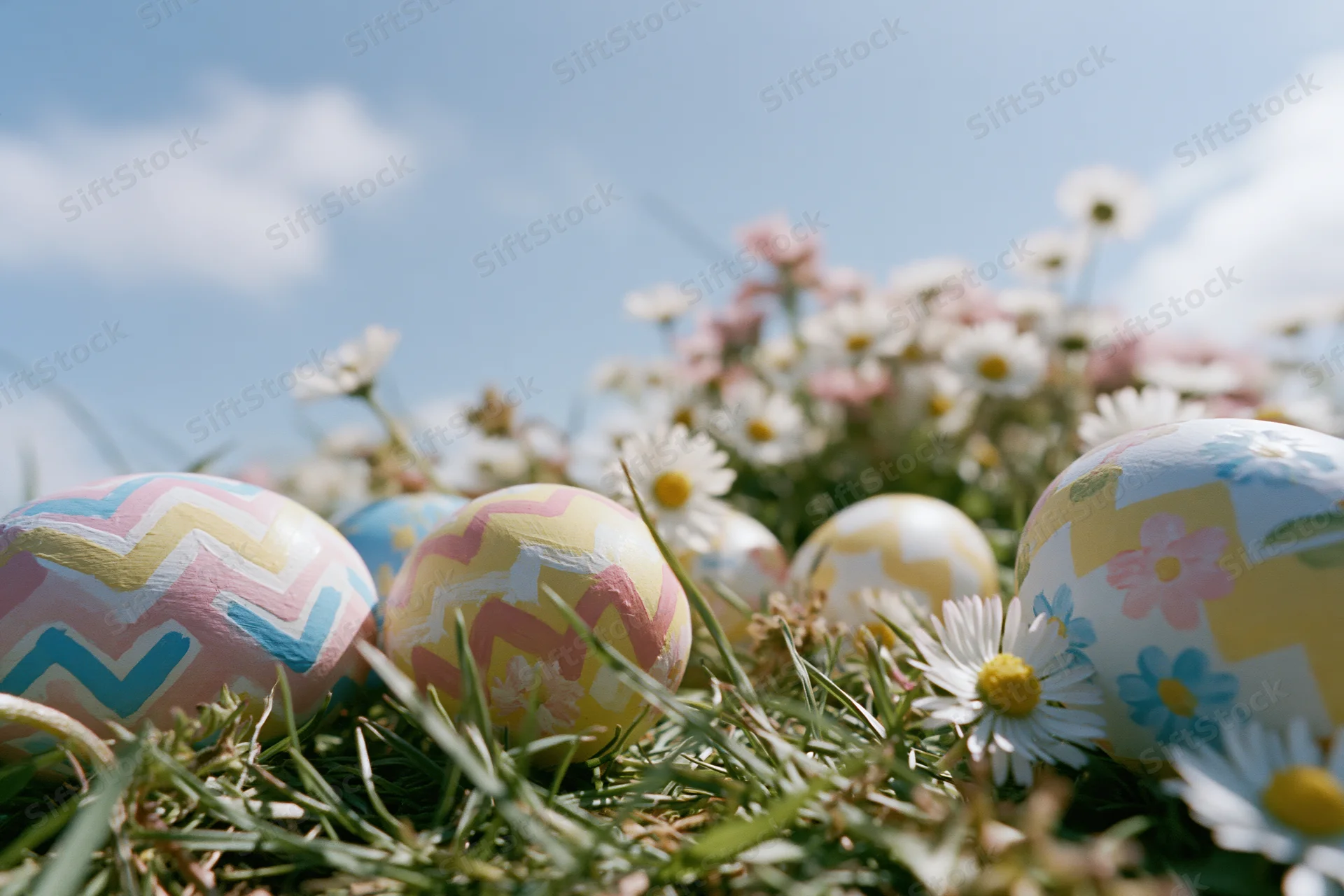 Decorated easter eggs resting in green grass among daisies under a blue sky