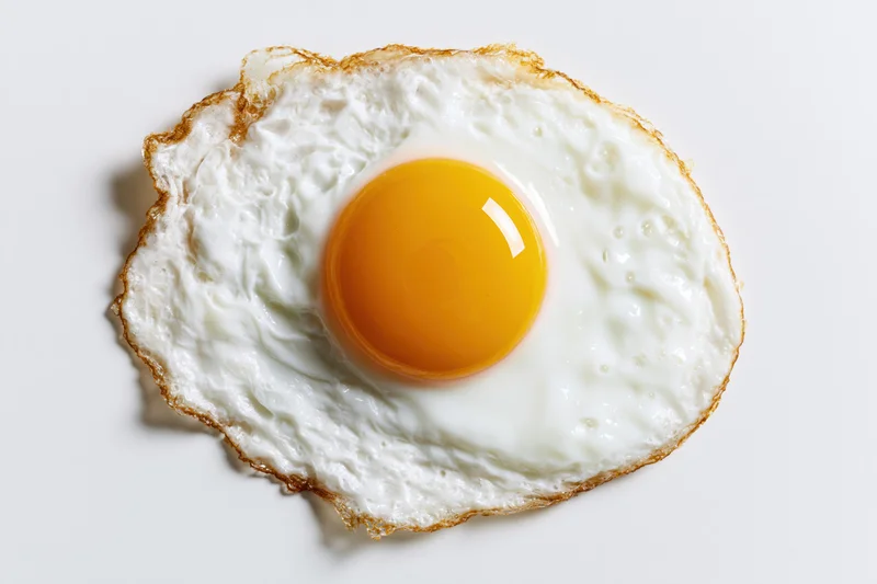 Single fried egg sunny side up viewed from directly above on white surface