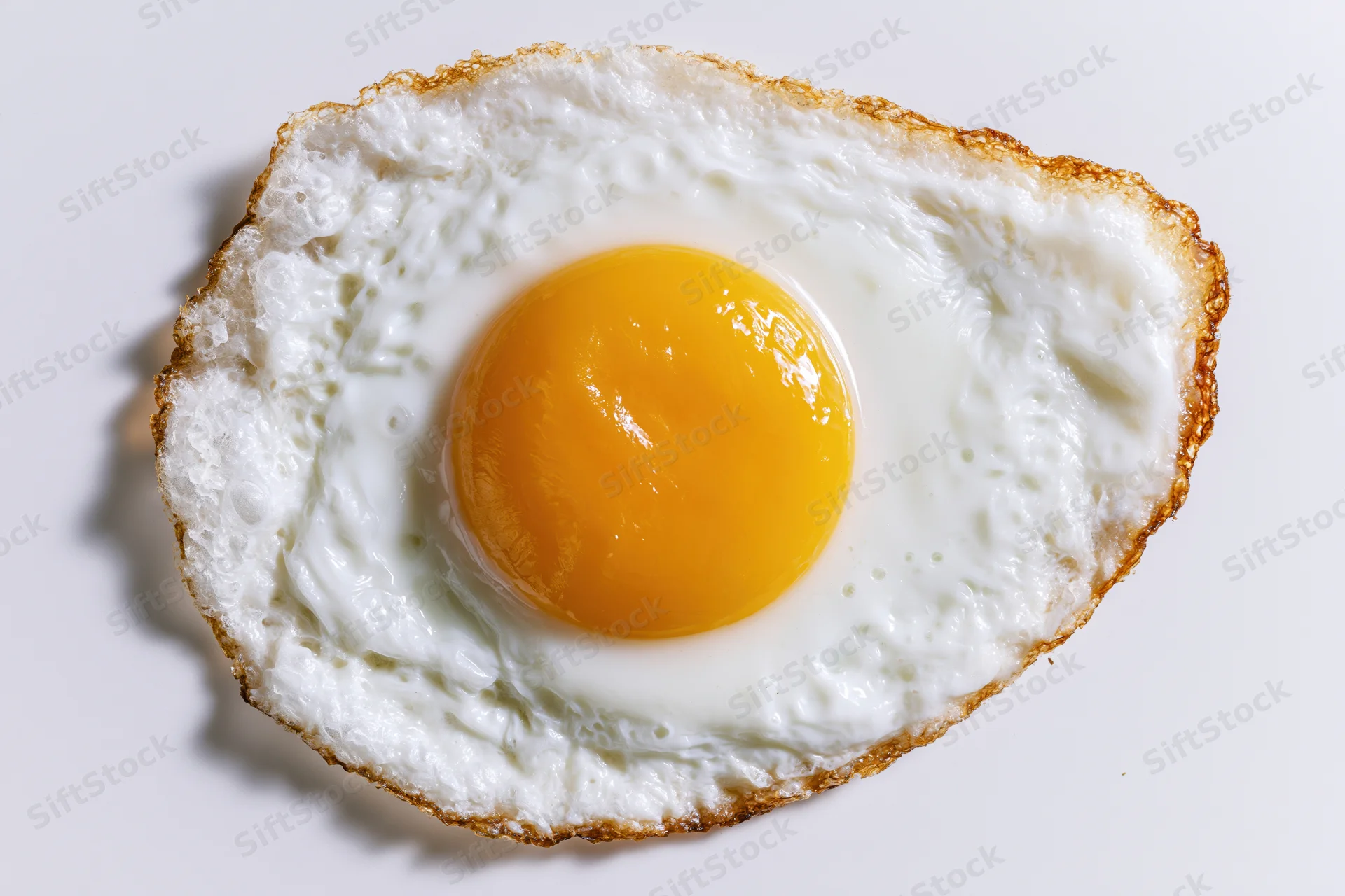 Single fried egg sunny side up shot directly overhead on a plain white surface