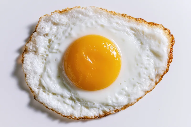 Single fried egg sunny side up shot directly overhead on a plain white surface