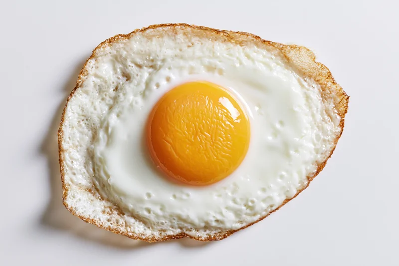 Single fried egg sunny side up viewed directly overhead on white surface
