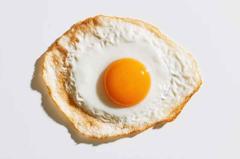 Single sunny-side-up fried egg viewed from directly above on white surface