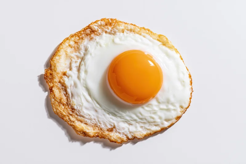 Single sunny-side-up fried egg viewed from directly overhead on white surface