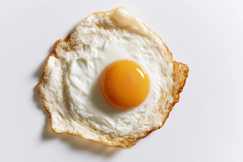 Single sunny-side-up fried egg viewed from directly overhead on white surface