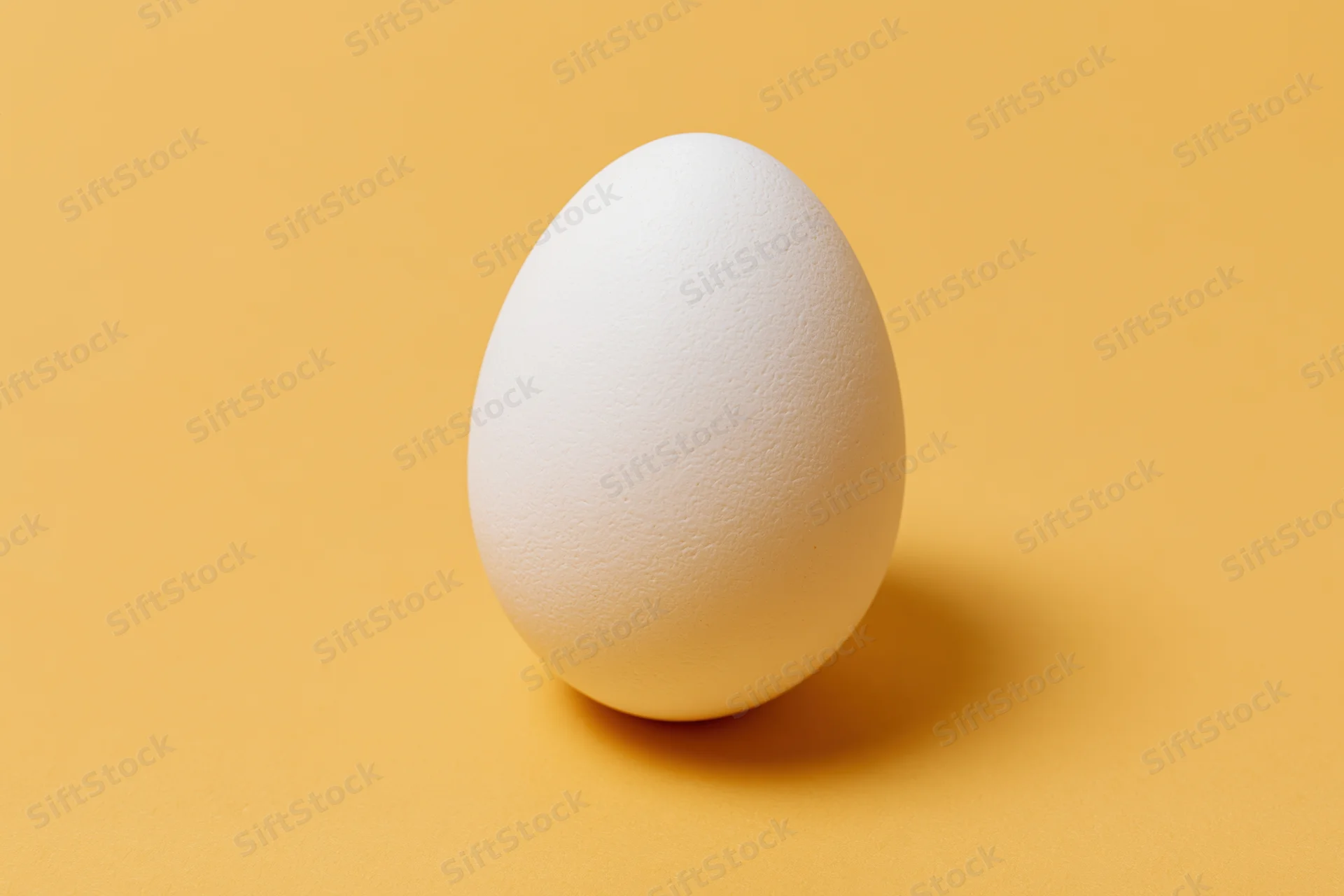 Single white chicken egg standing upright centered on yellow background