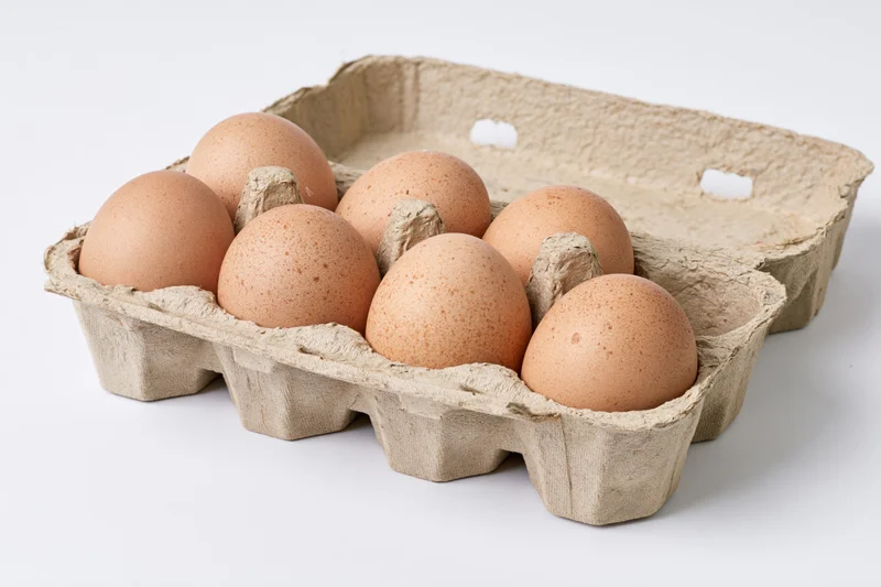 Six brown chicken eggs arranged in an open recycled cardboard carton on a white background