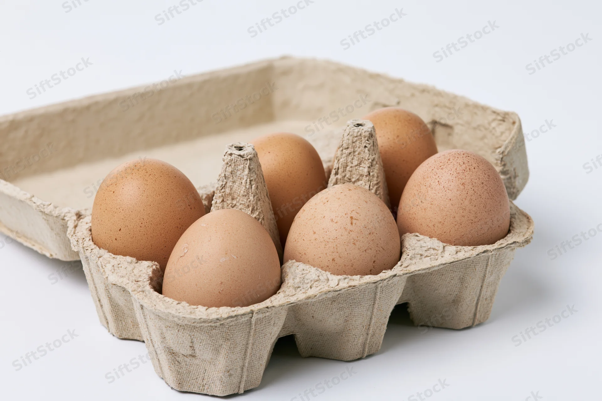 Six brown chicken eggs arranged in an open recycled cardboard carton on a white surface