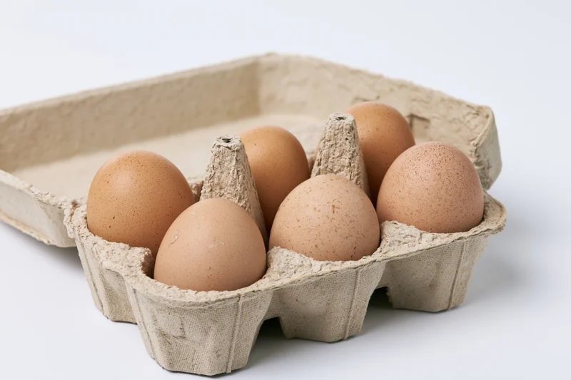 Six brown chicken eggs arranged in an open recycled cardboard carton on a white surface