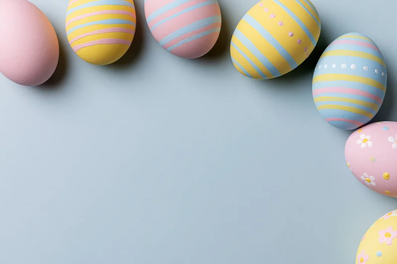 Decorated easter eggs arranged along the top and right edge of a light blue surface with copyspace
