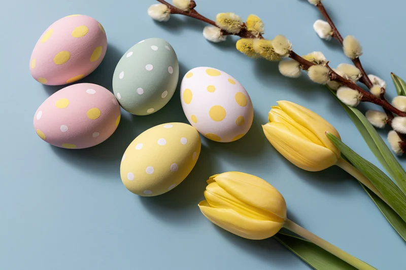 Decorated easter eggs with tulips and willow branches arranged on a blue background
