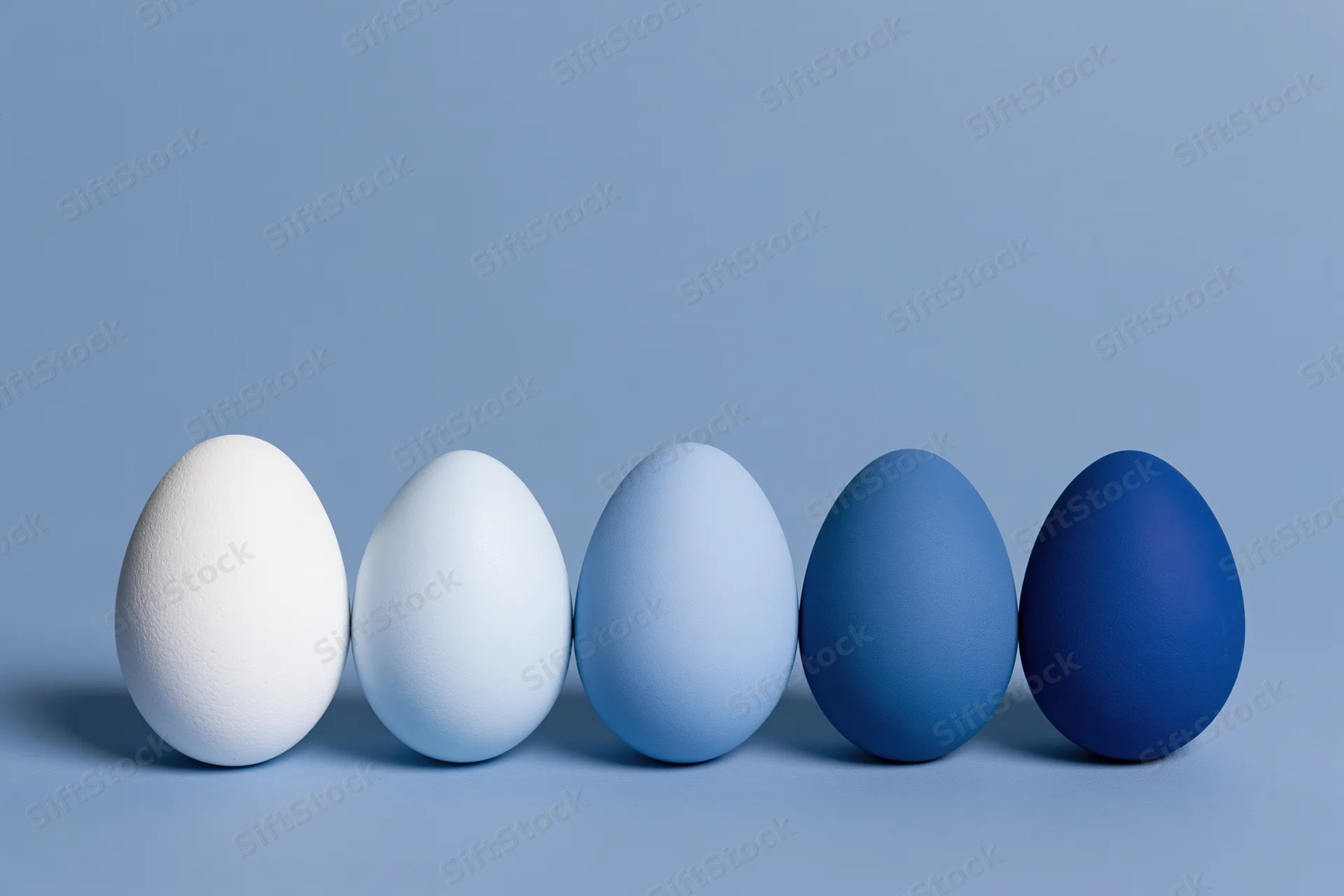 Five eggs in a row graduating from white to blue on a flat surface