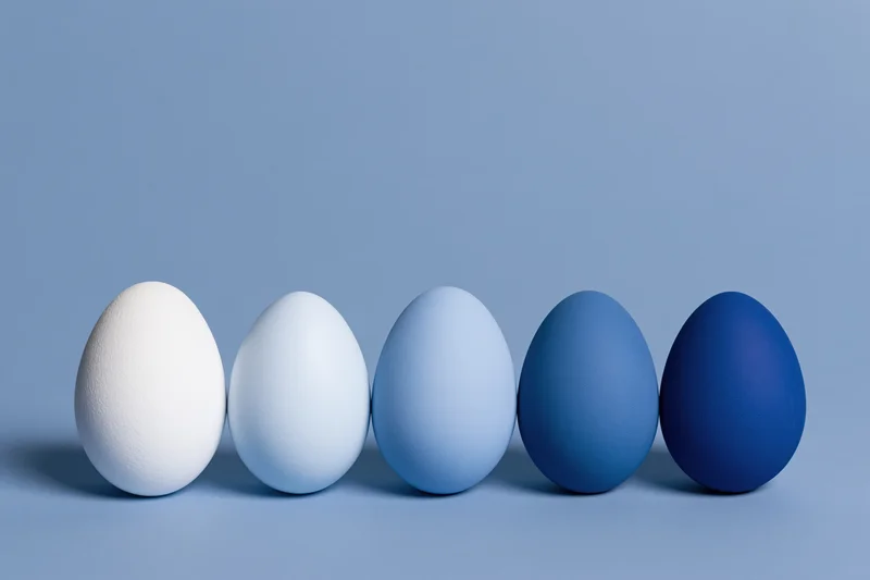 Five eggs in a row graduating from white to blue on a flat surface