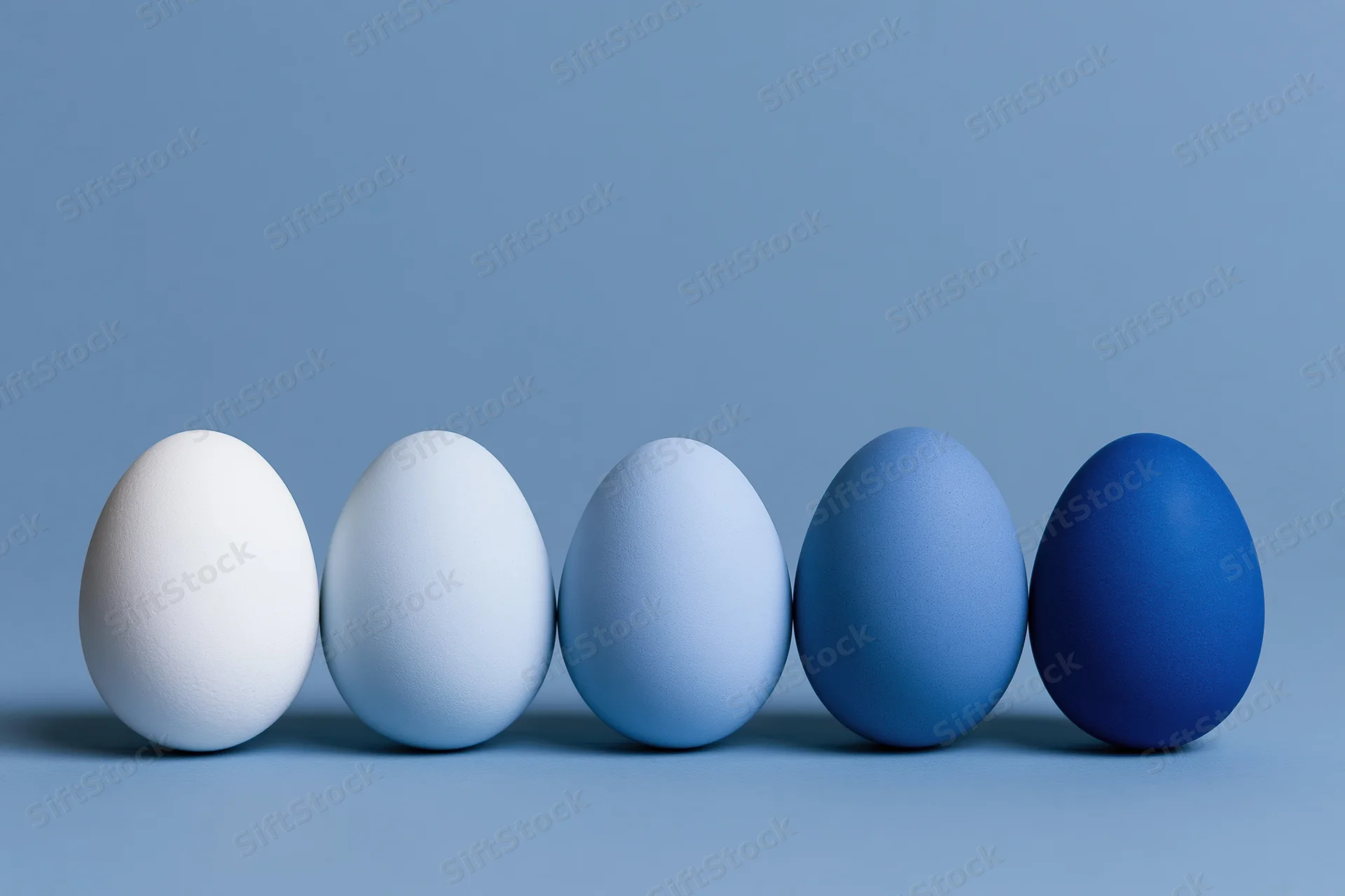 Five eggs in a row graduating from white to blue on a flat surface