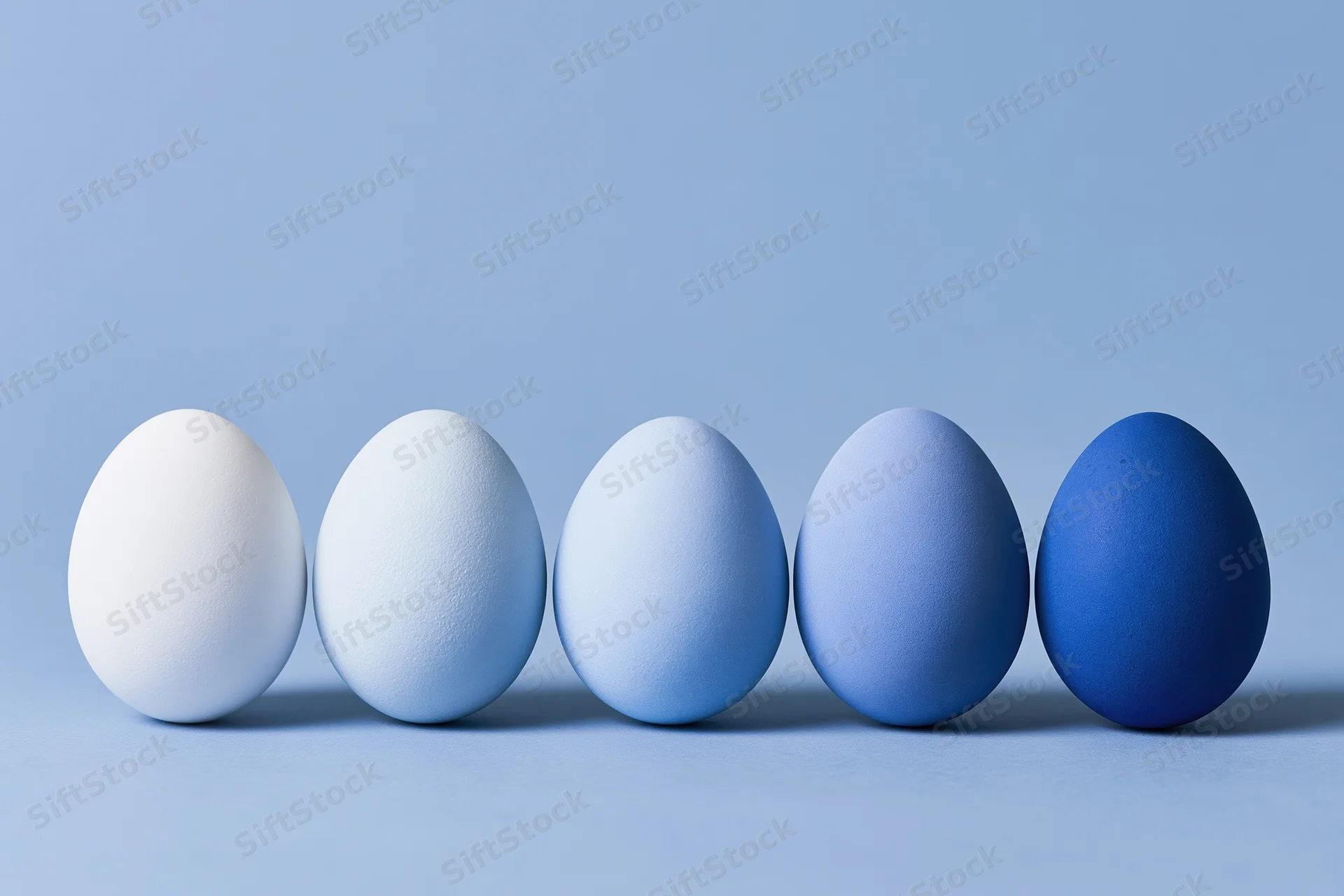 Five eggs in a row graduating from white to blue on a flat surface