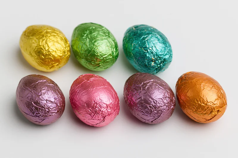 Foil-wrapped chocolate easter eggs arranged in two rows on white background