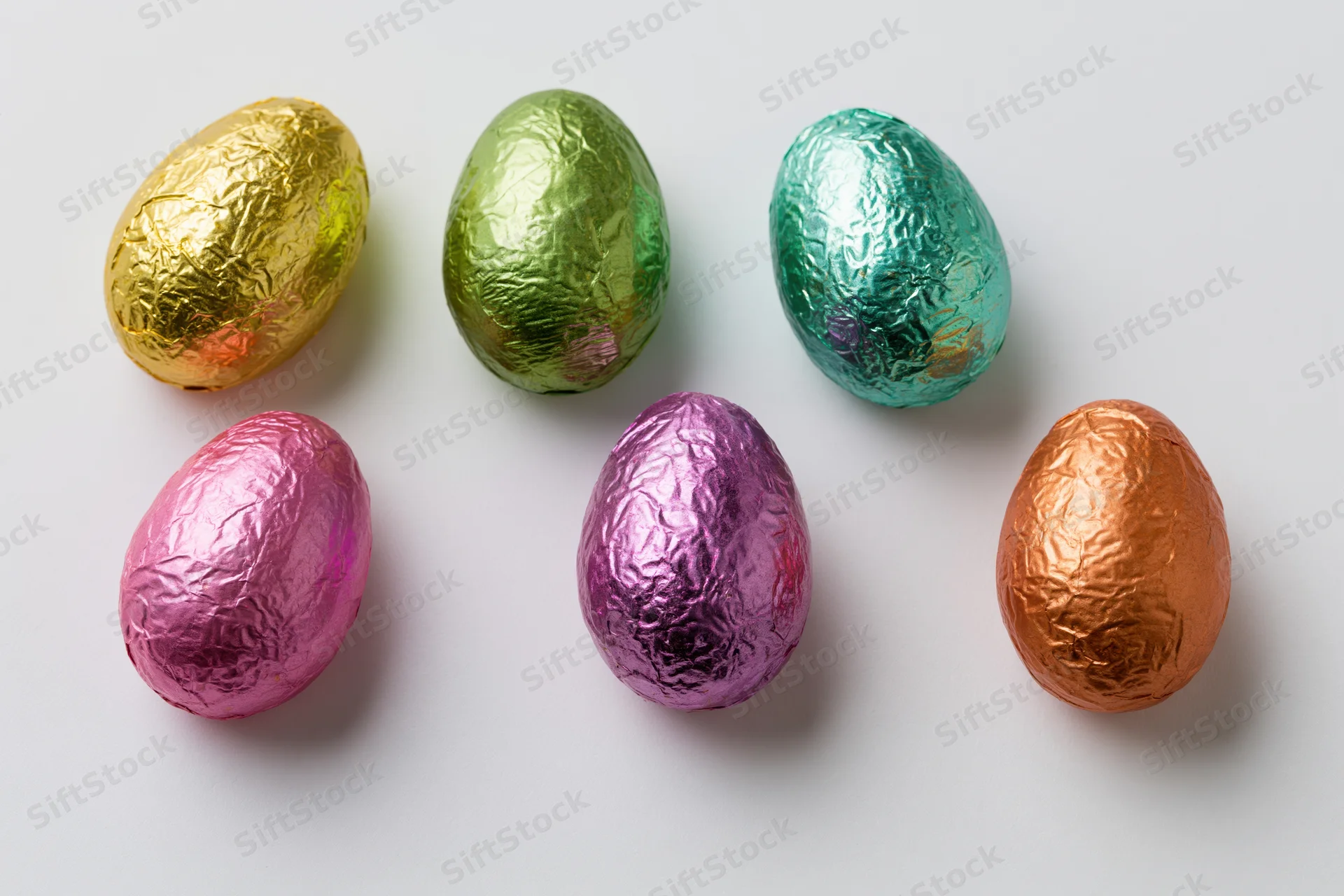 Six foil-wrapped chocolate easter eggs arranged in two rows on white background