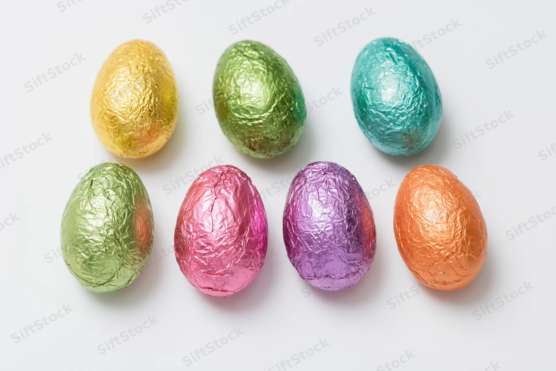 Foil-wrapped chocolate easter eggs arranged in two rows on white background