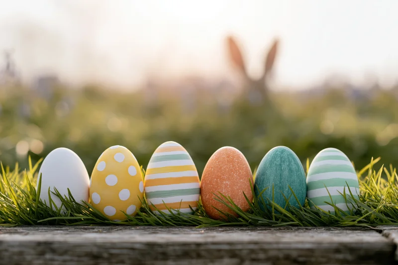 Six painted easter eggs arranged in a row on green grass atop a wooden surface with blurred background and copyspace