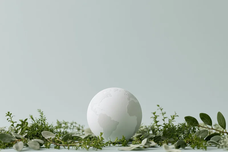Matte white globe model resting on a bed of green herbs and leaves on a flat surface