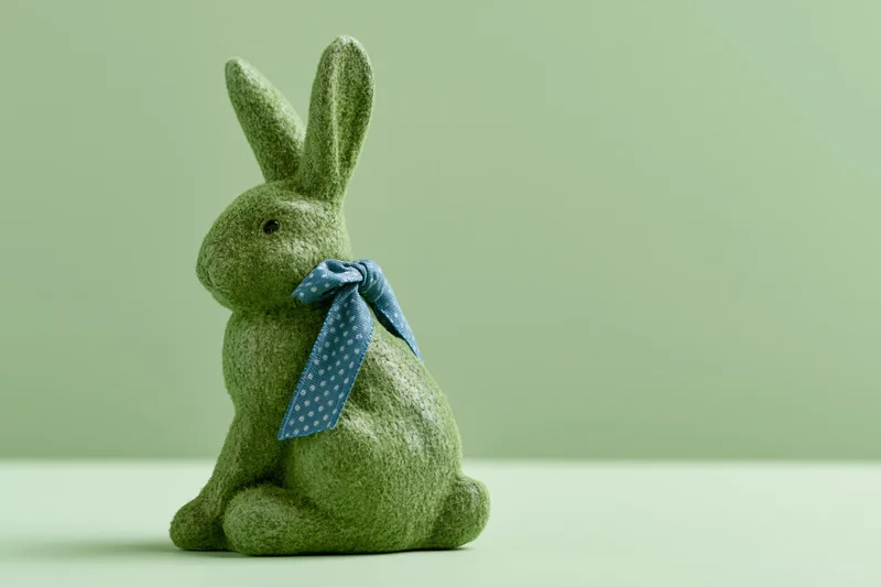 Moss-textured ceramic easter bunny figurine sitting upright with blue polka dot ribbon on light green background