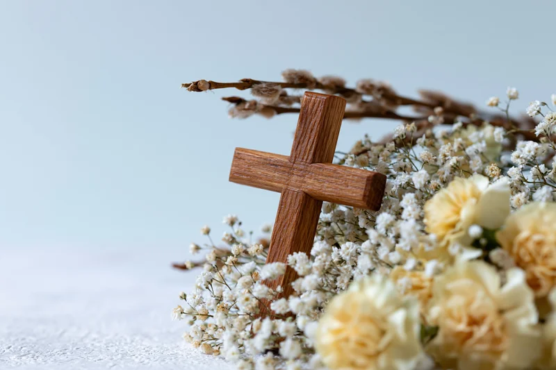 Wooden cross resting among white and cream flowers on a light surface