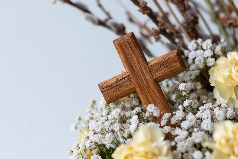 Wooden cross resting on a bouquet of white baby's-breath and yellow carnations with dried lavender stems