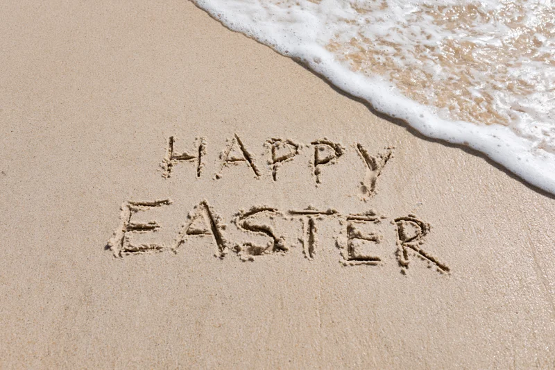 Happy easter written in wet sand on a beach with waves approaching