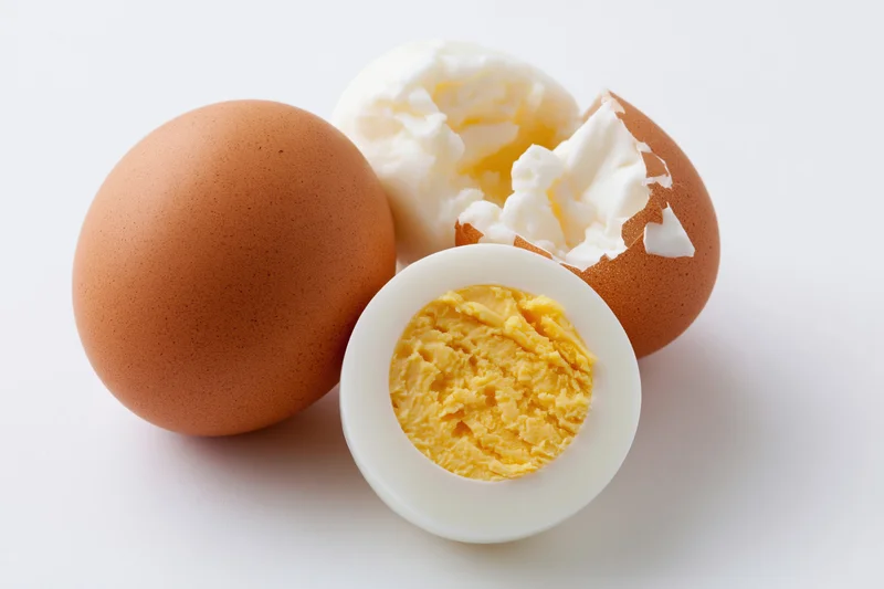 Three boiled eggs arranged on a white surface, one whole unpeeled, one halved showing yolk, one partially peeled
