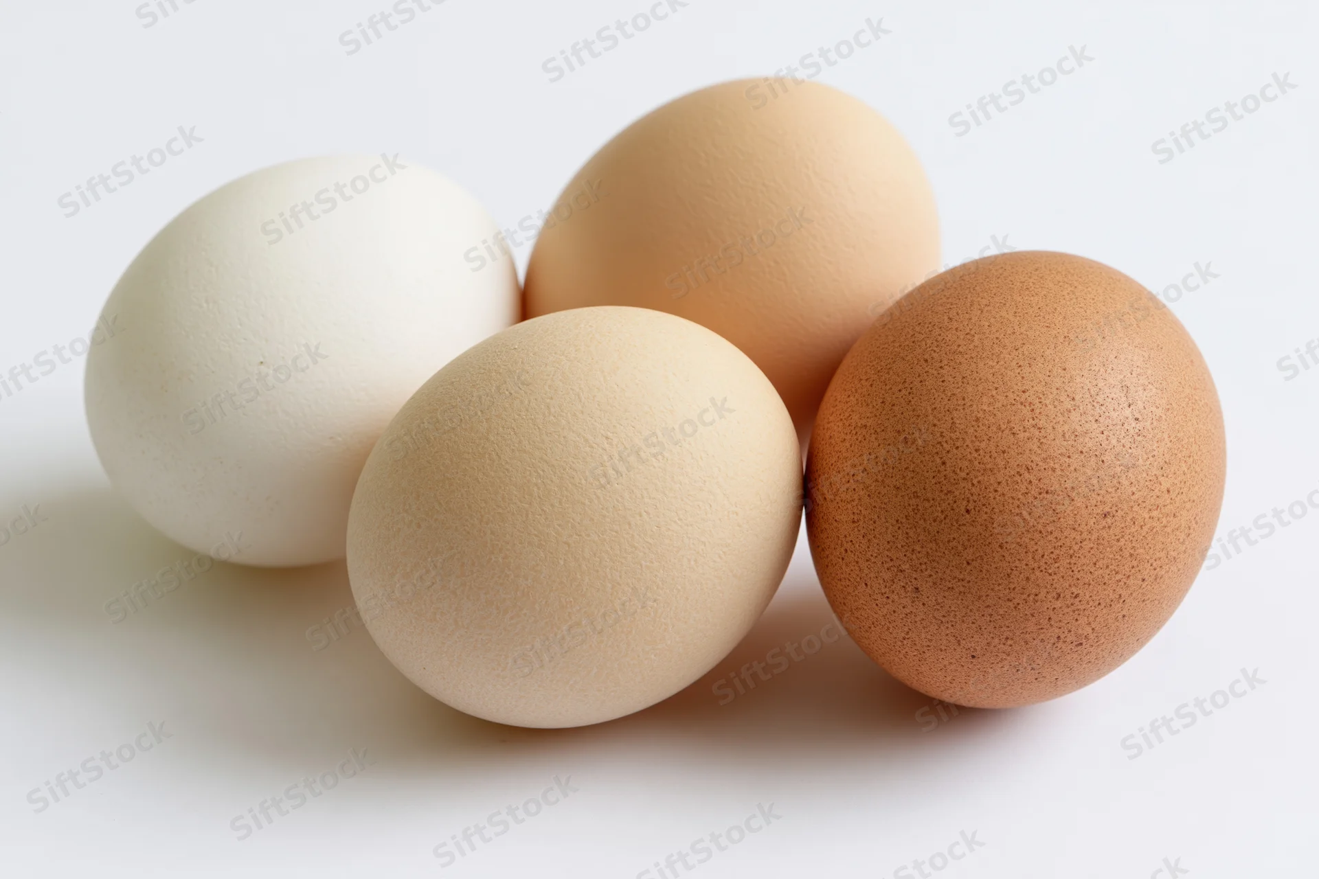 Four chicken eggs arranged loosely together on a white surface, varying in shell color from white to brown
