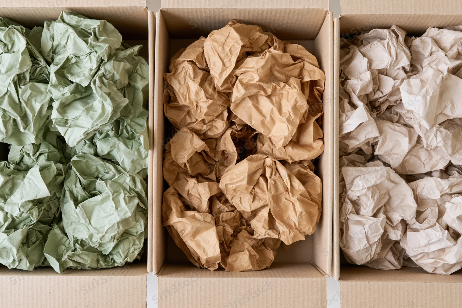 Three open cardboard boxes filled with crumpled paper in green, brown and white, arranged side by side