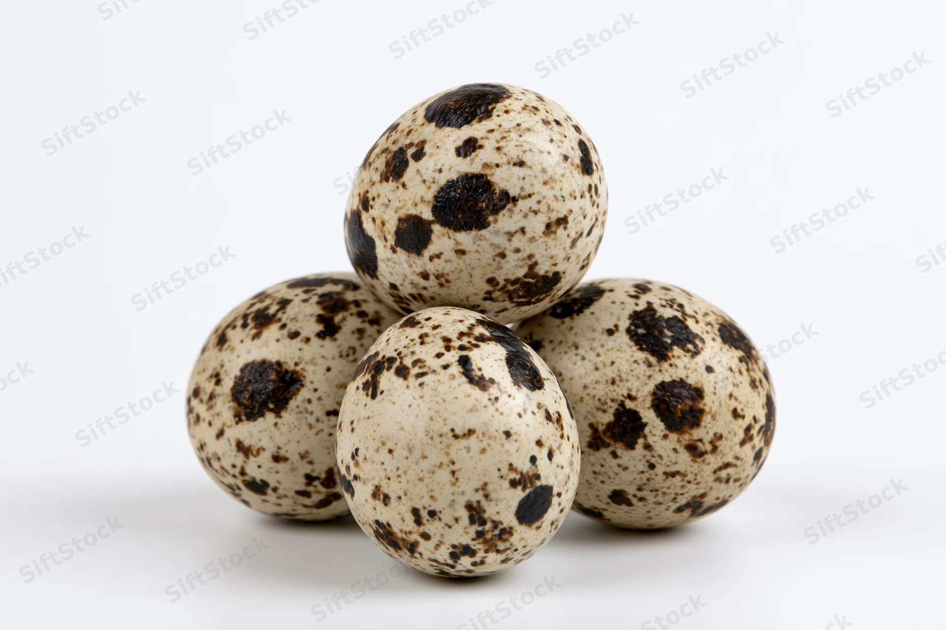 Quail eggs arranged in a loose pyramid on a white surface