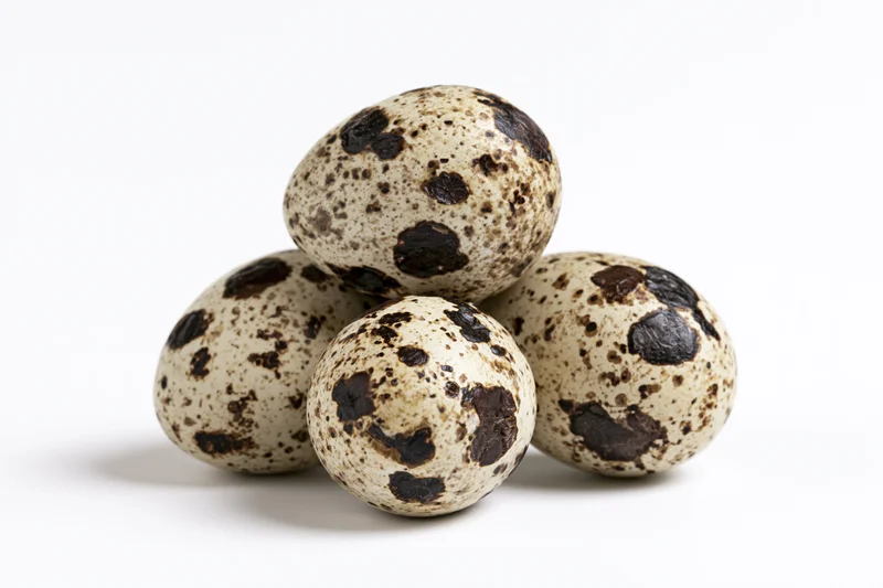 Quail eggs stacked in a loose pyramid arrangement on white background